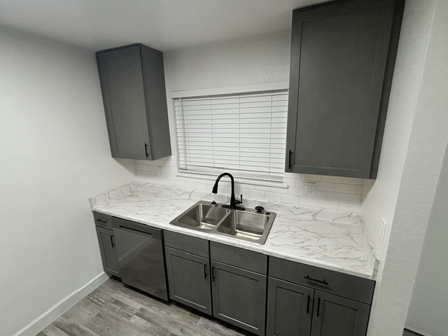 Remodeled apartment kitchen with grey cabinets, marble-look countertop, and new sink