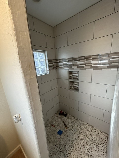 Finished tiled shower showing built-in niche, accent band, and glass block window